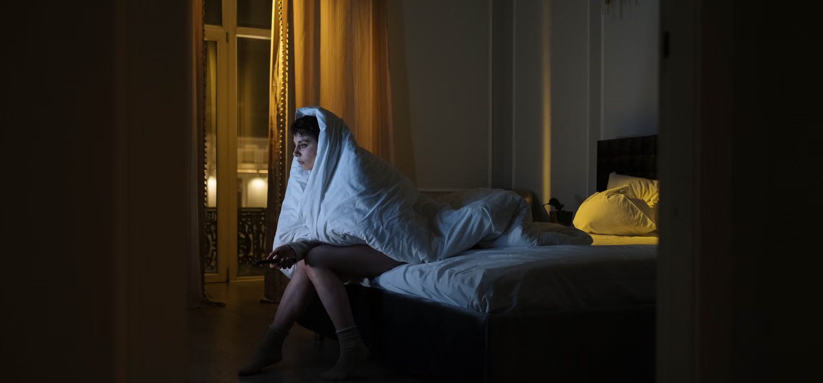 A woman lying awake in a dark bedroom, lit by a screen